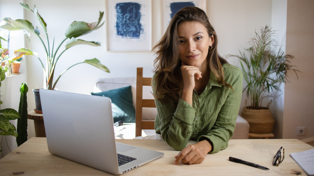 Donna che lavora in smart working seduta alla scrivania con laptop, piante e documenti, in un ambiente domestico luminoso e accogliente.