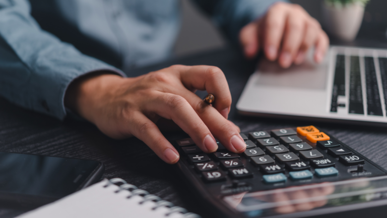 Payroll cos'&egrave; e fasi. Mano che utilizza una calcolatrice su una scrivania per calco buste paga